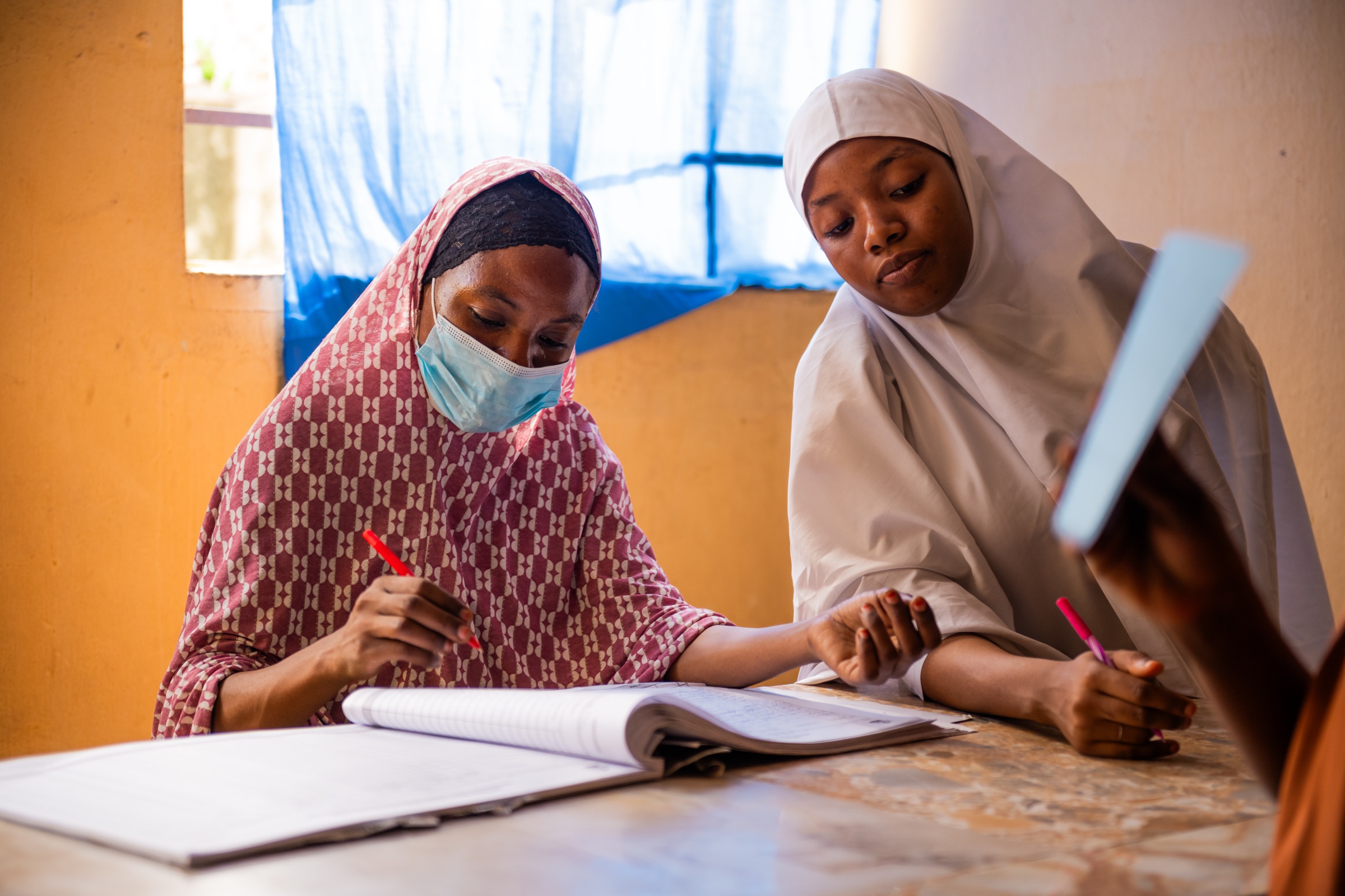 Two health workers reviewing a facility register